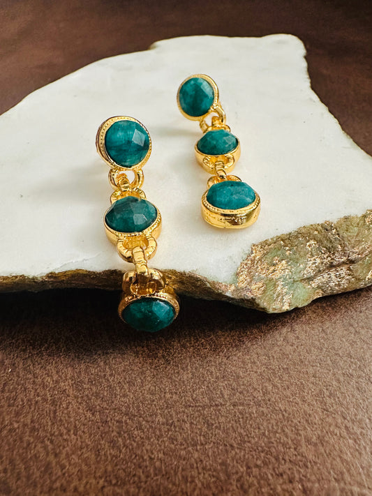 Handmade Gold-plated earrings with emerald gemstones on a stone surface