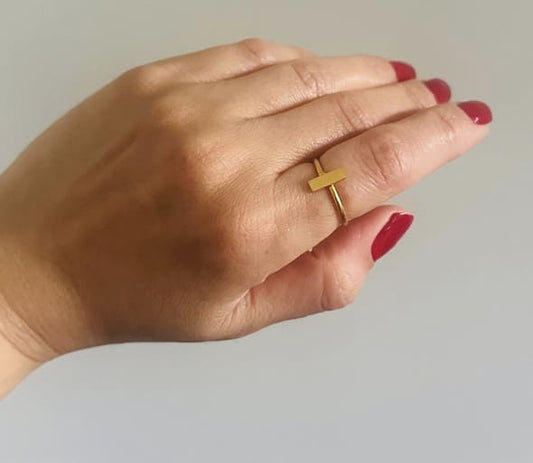 Hand wearing a Handmade gold-plated waterproof bar ring with red nail polish on a neutral background