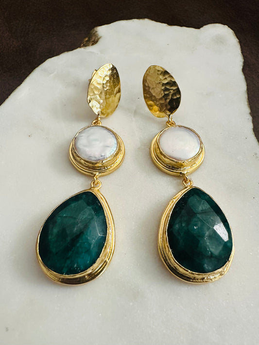 Gold earrings with green and white stones on a marble surface
