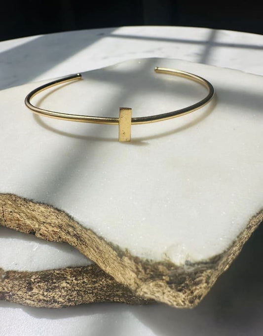 Dainty stackable Gold-plated bracelet with minimal bar on a white marble surface