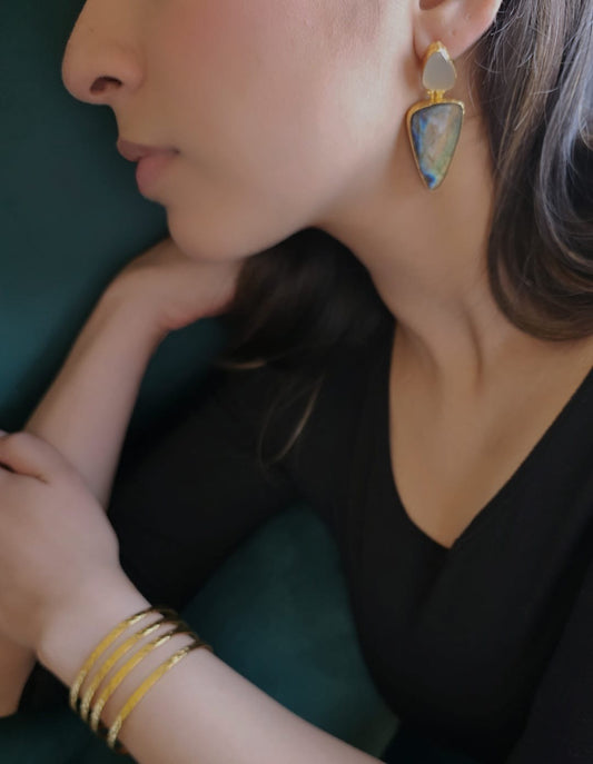 Close-up of a person wearing gold earrings and bracelets against a dark background