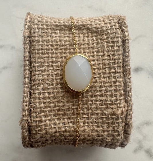 Minimal handmade gold-played chain bracelet with a snow Quartz pendant on a textured beige fabric against a marble background