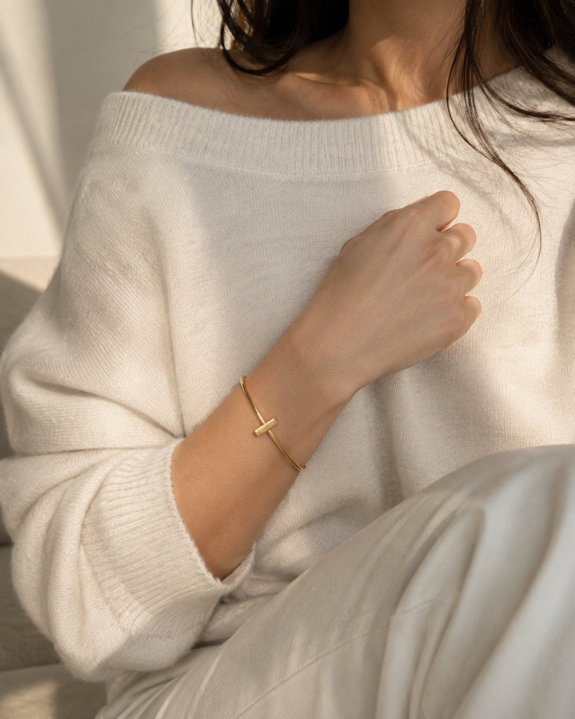 Up close view of model wearing oversized off-white sweater by Aritzia and a handmade gold-plated minimal bar bracelet 