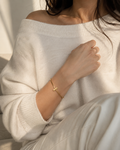 Up close view of model wearing oversized off-white sweater by Aritzia and a handmade gold-plated minimal bar bracelet 