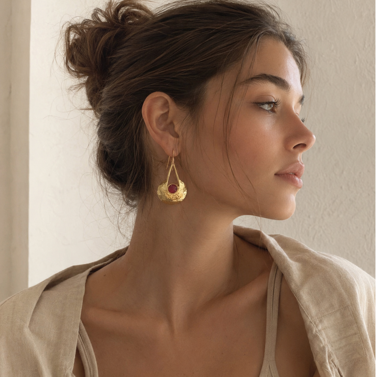 A close-up image of a woman wearing gold high end gold-plated ruby earrings And beige outfit from Aritzia