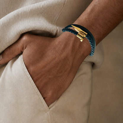 A close-up of a person's hand resting in a beige pocket, wearing navy braided leather bracelet with a gold-toned metal accent.