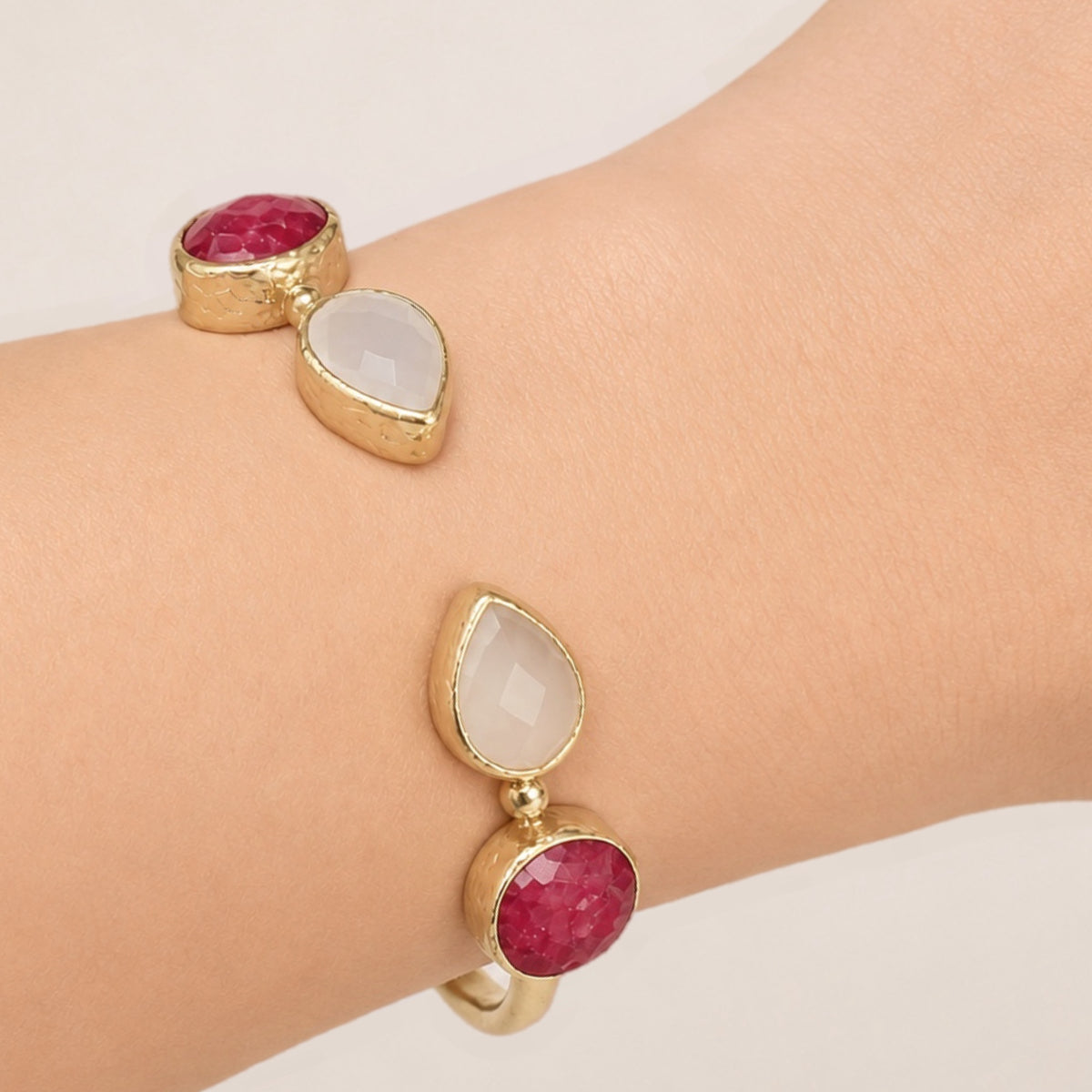 A close-up of a person's wrist wearing m gold-plated snow Quartz and Ruby adjustable cuff bracelet.