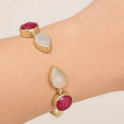 A close-up of a person's wrist wearing m gold-plated snow Quartz and Ruby adjustable cuff bracelet.