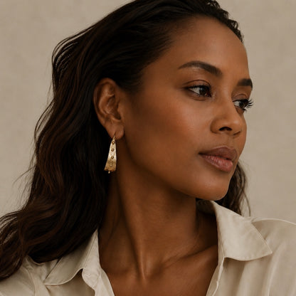A close up of an African American model with beige button up satin shirt and gold contemporary earrings 