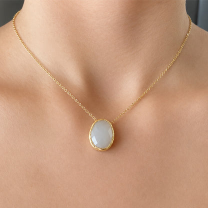 A gold chain necklace with a faceted oval snow Quartz pendant, worn on a model's neck.