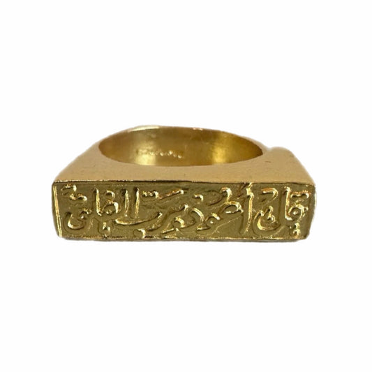 A gold-plated bar ring with Arabic calligraphy engraved on it, displayed on a white surface