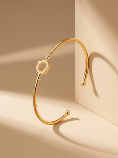 A gold-plated brass cuff bracelet with a central open hexagon design upright on a plain beige background.