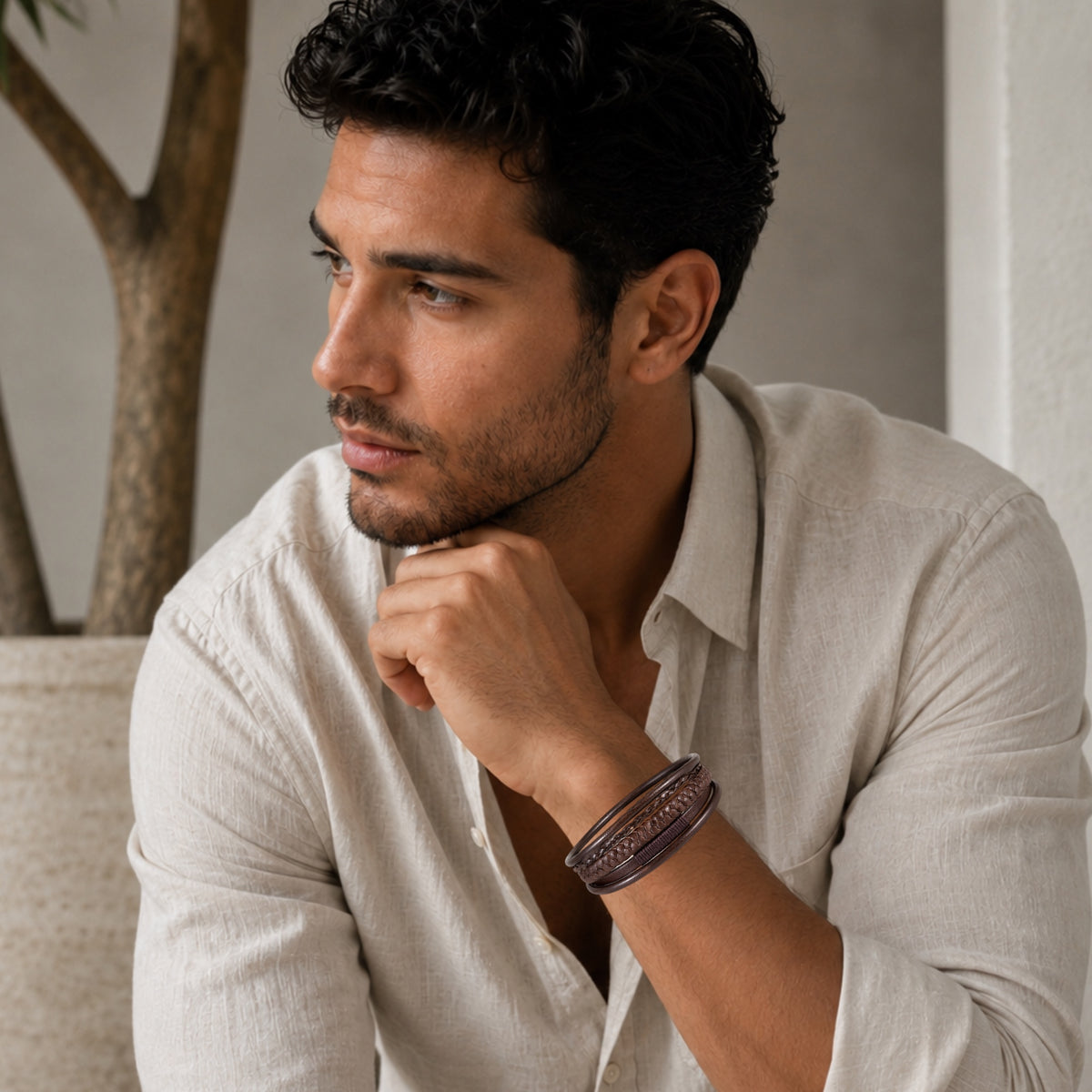 A man wearing a boho chick brown woven leather bracelet, posing in a light beige linen shirt in a softly lit indoor setting.