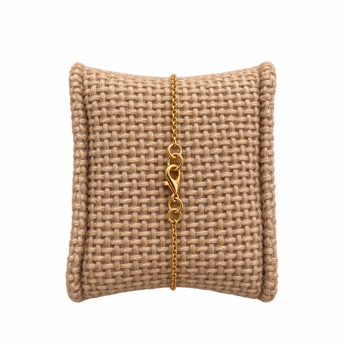 A minimal gold chain bracelet with a lobster clasp, displayed on a woven beige jewelry pillow against a white background.