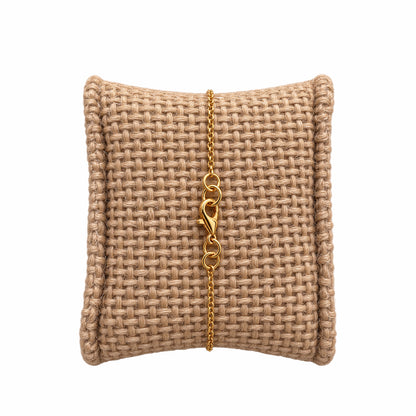 A minimal gold chain bracelet with a lobster clasp, displayed on a woven beige jewelry pillow against a white background.