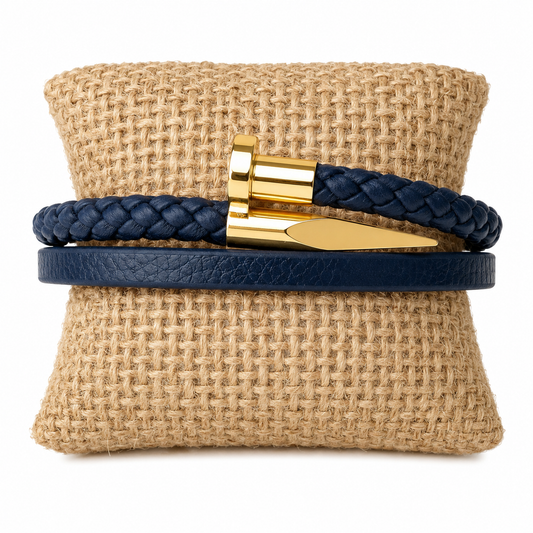 A navy blue leather wrap bracelet with a gold-nail design and gold clasp, displayed on a textured tan burlap cushion against a white background.