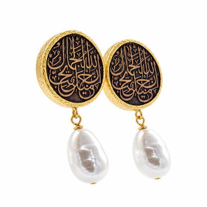 A pair of gold and black drop earrings featuring circular studs with Arabic calligraphy and dangling baroque white pearls on a white background facing right 