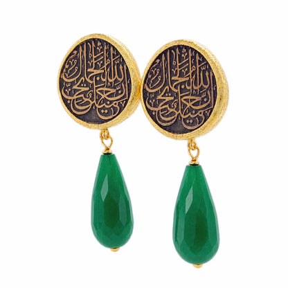 A pair of gold and black drop earrings featuring circular studs with Arabic calligraphy and dangling green Jade on a white background facing left