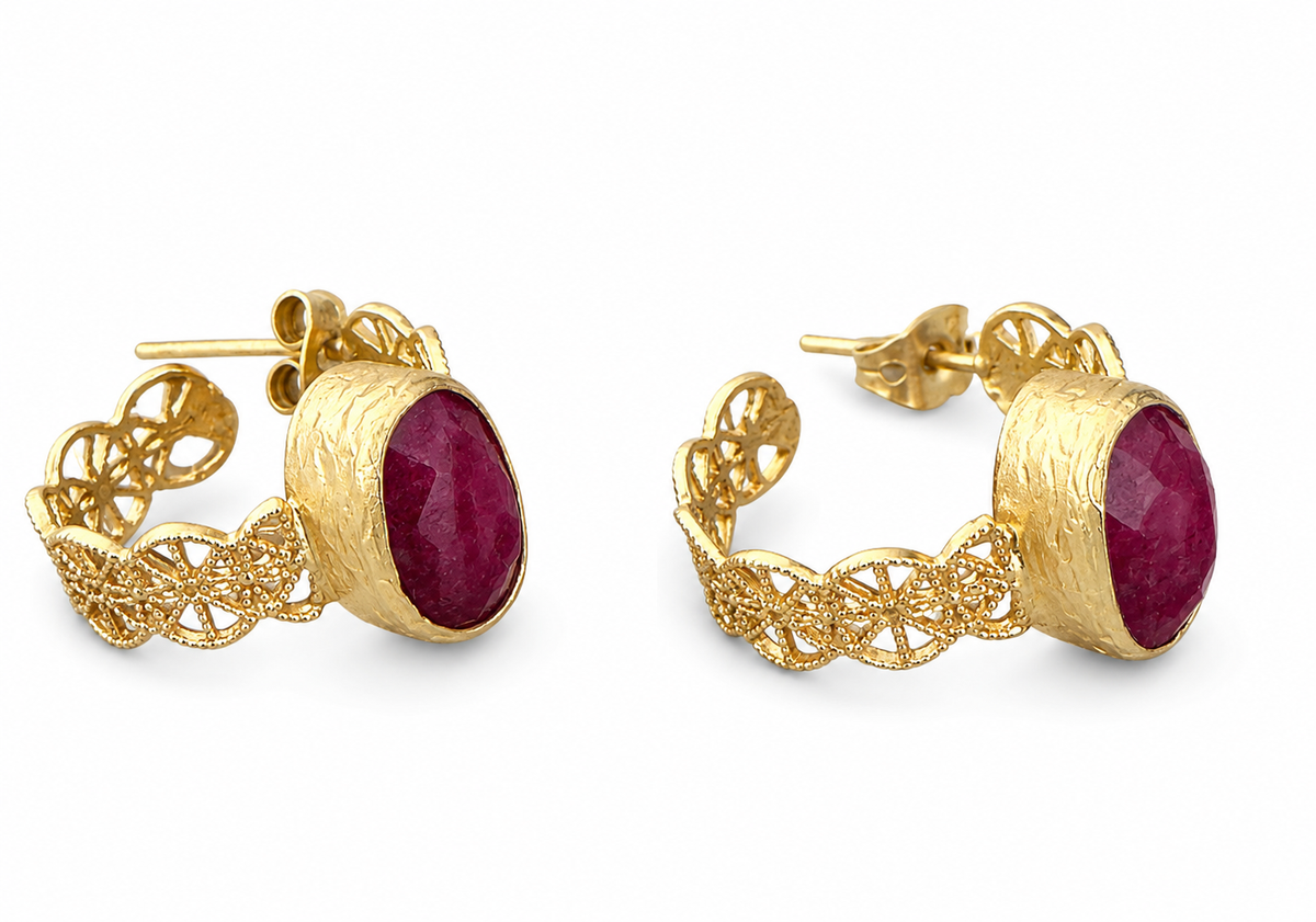 A pair of gold hoop earrings with textured gold bands, intricate filigree details, and oval dark red rubygemstone centers, shown on white background.