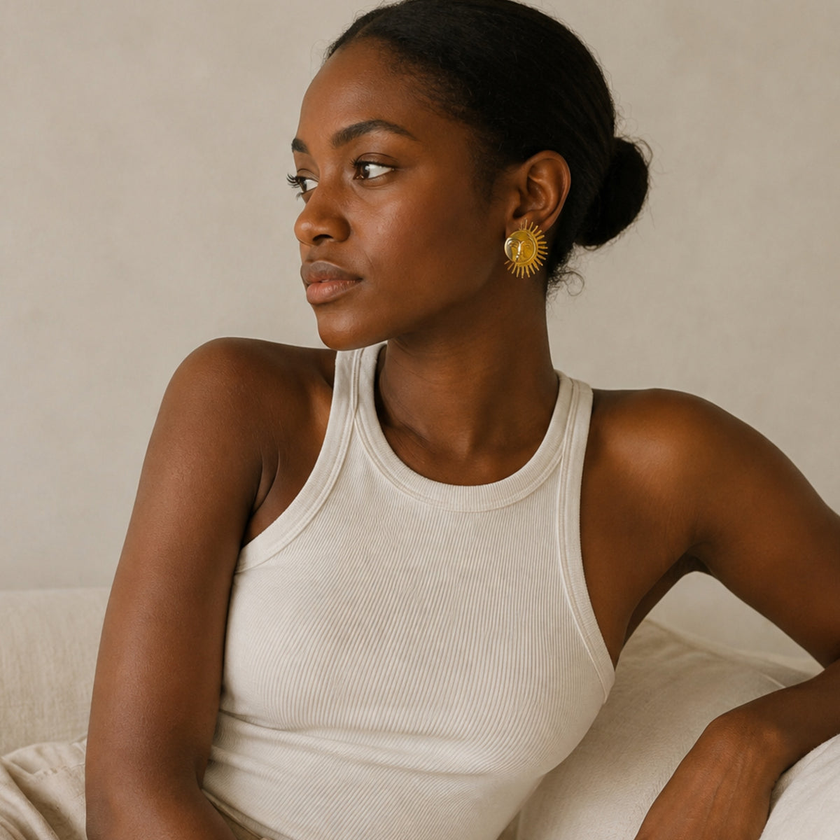 A pair of gold-plated sun stud earrings worn by model against a beige background.