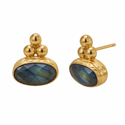 A pair of gold stud earrings featuring oval faceted labradorite stones with blue-green iridescent sheen, set in a textured gold bezel with three small gold beads above.