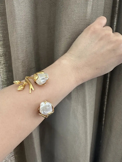 Arm wearing baroque pearl floral cuff bangle agajnst dark background 