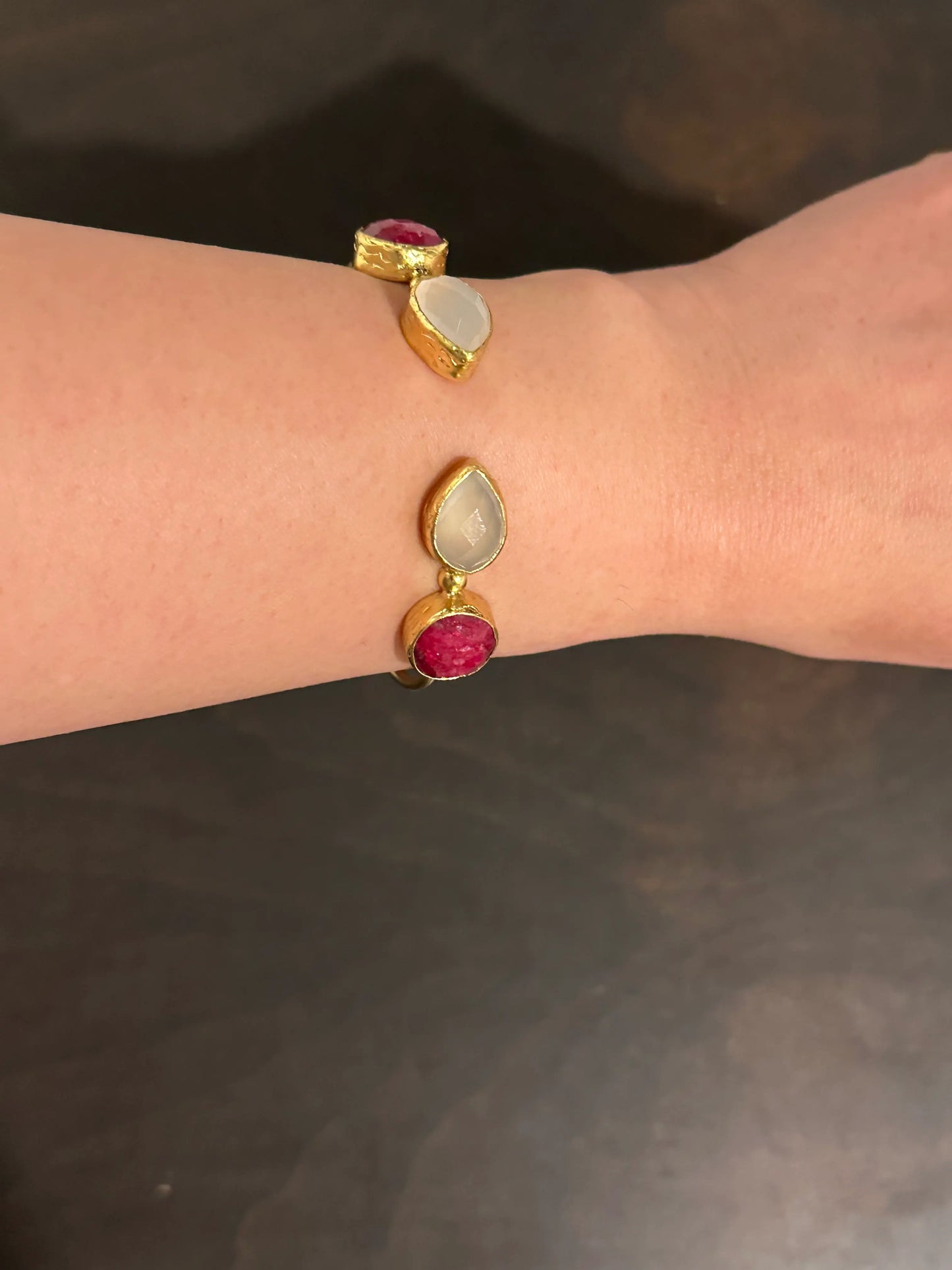 Gold ruby multi-stone bracelet with gemstones on a wrist against a dark background