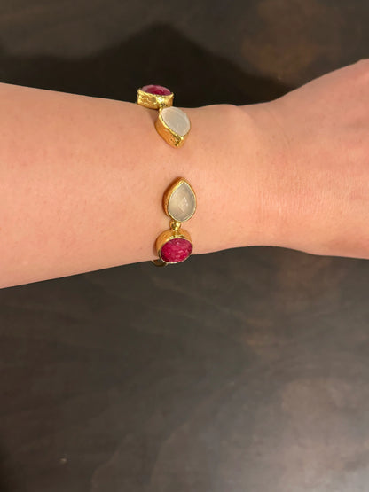 Gold ruby multi-stone bracelet with gemstones on a wrist against a dark background