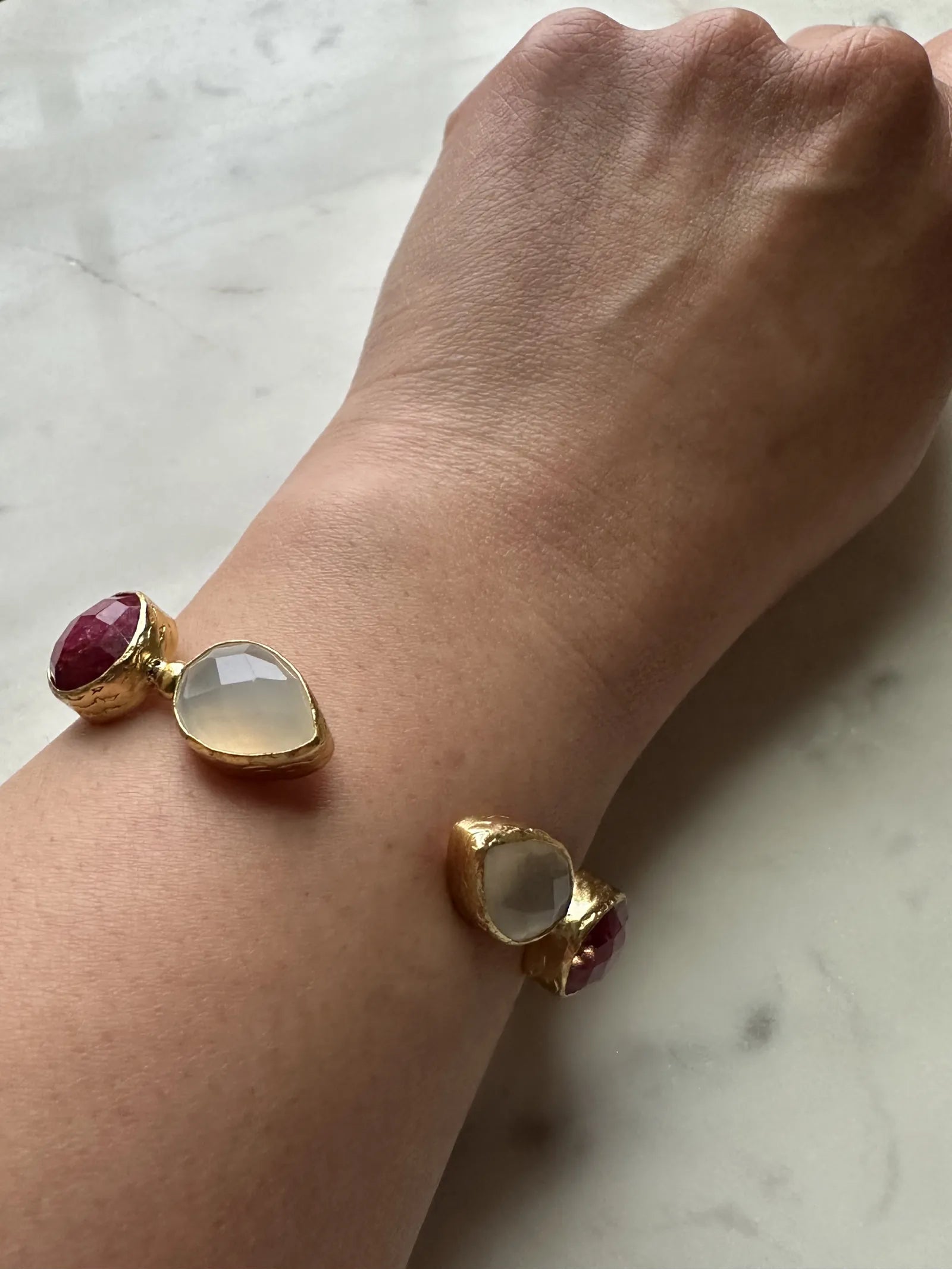 Arm wearing artisanal Gold bracelet with Ruby gemstones on a wrist against a marble background