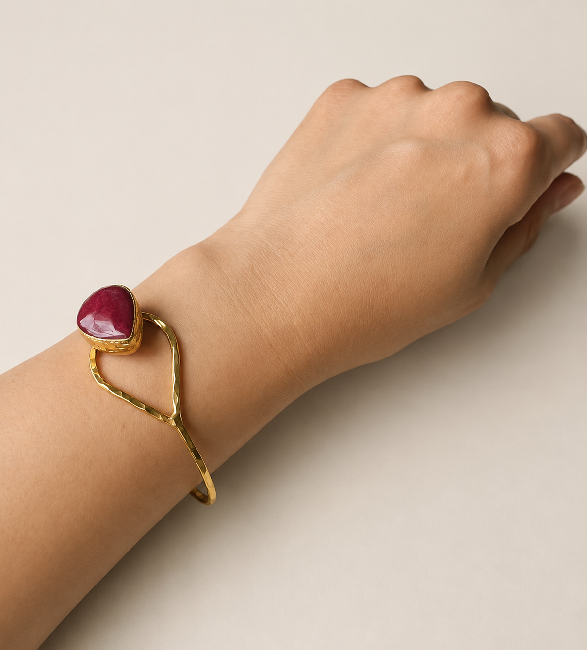 Arm wearing Artisanal Gold-plated hammer-finished bracelet with a red ruby gemstone on a white surface