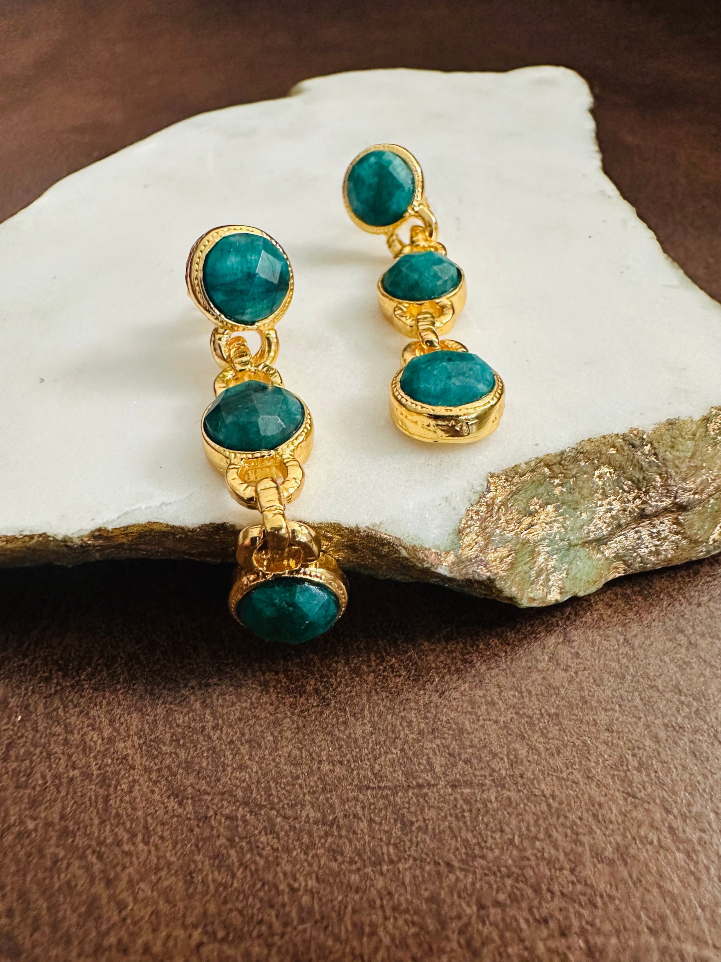 Handmade Gold-plated earrings with emerald gemstones on a stone surface