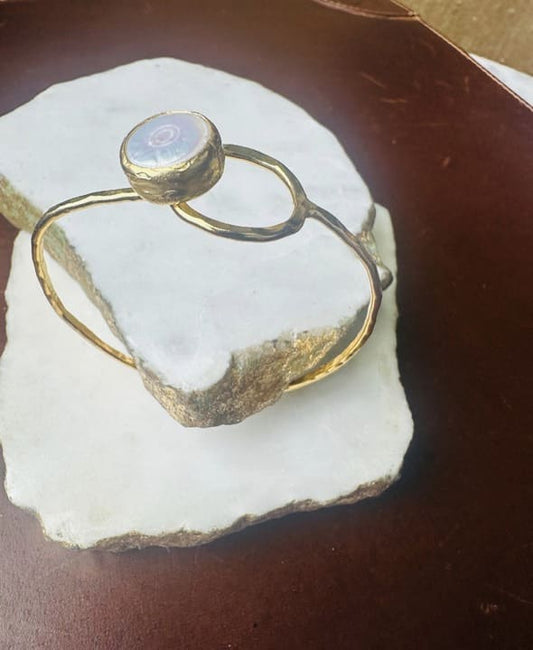 Gold-plated bracelet with loop and a flat pearl stone on a white stone surface