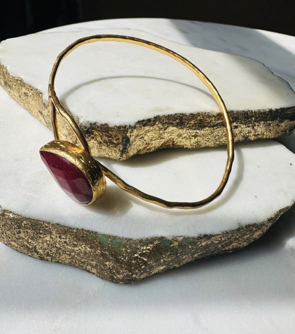 Gold-plated handmade hammer-finished cuff bangle with a loop and ruby on white surface