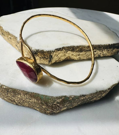 Gold-plated handmade hammer-finished cuff bangle with a loop and ruby on white surface