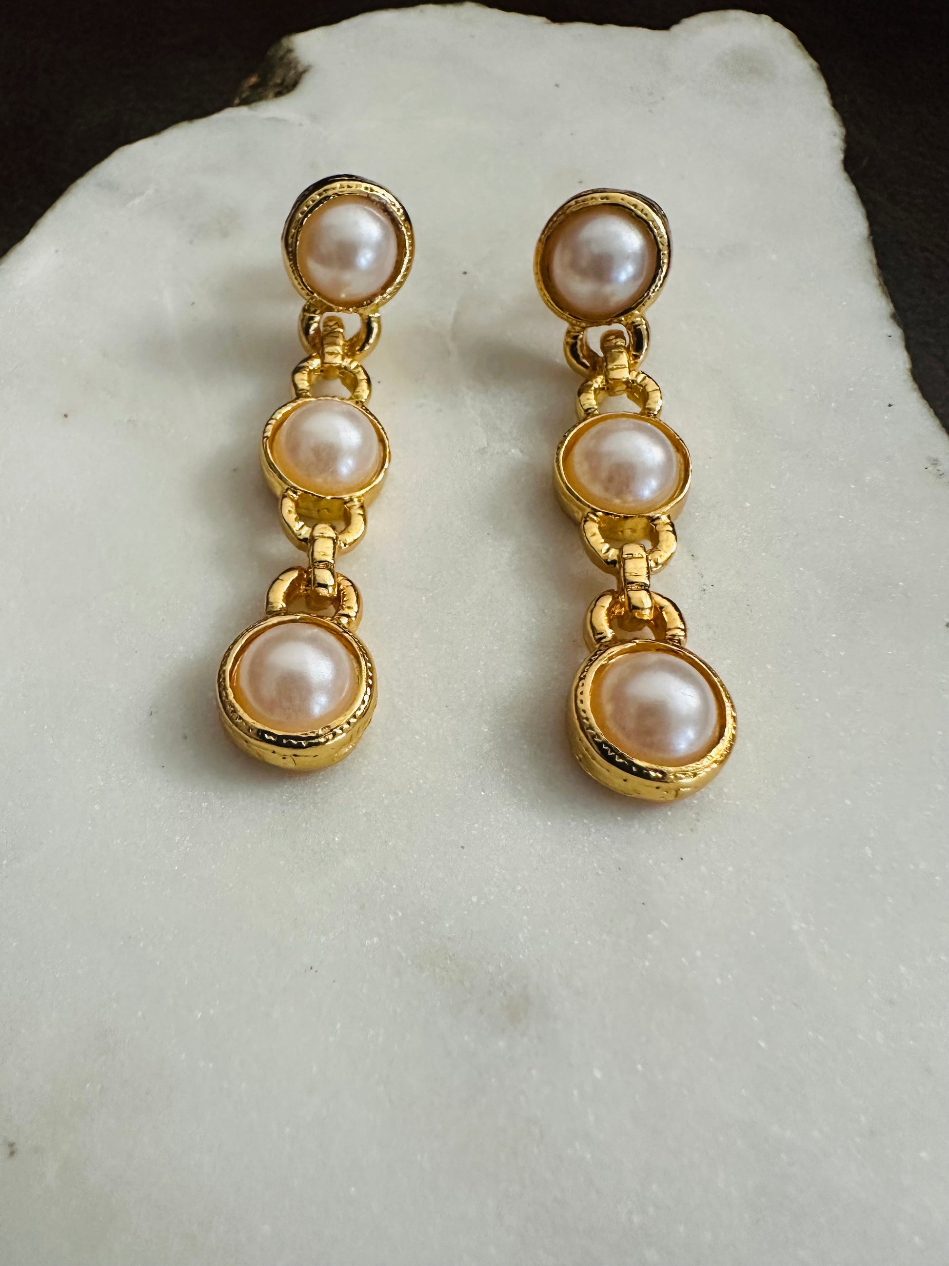 Pair of gold earrings with pearl drops on a white stone surface