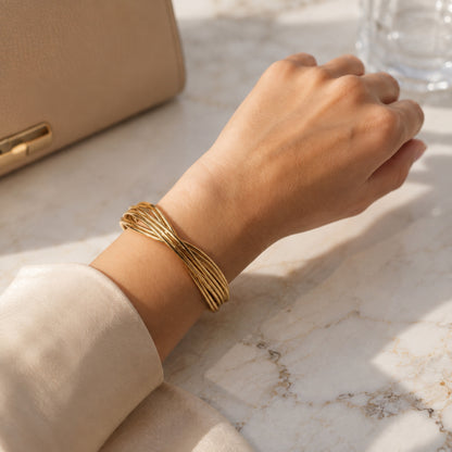 Gold-plated wire cuff bracelet on a woman’s wrist against a marble background