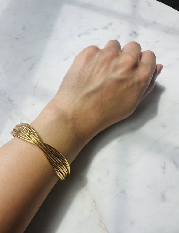 Gold-plated wire cuff bracelet on a wrist against a marble background