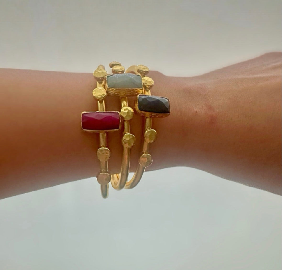 Gold-plated sustainable bracelet stacks with ruby, lapis lazuli, and labradorite gemstones on a wrist against a neutral background