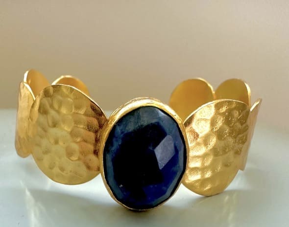 Gold-plated artisanal bracelet with a central blue lapis lazuli gemstone on a light background