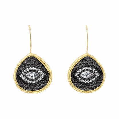 A pair of gold and dark silver teardrop-shaped drop earrings with a hammered gold finish, a textured center, and a central clear zircon evil  eye gemstone surrounded by small clear stones, on white background.