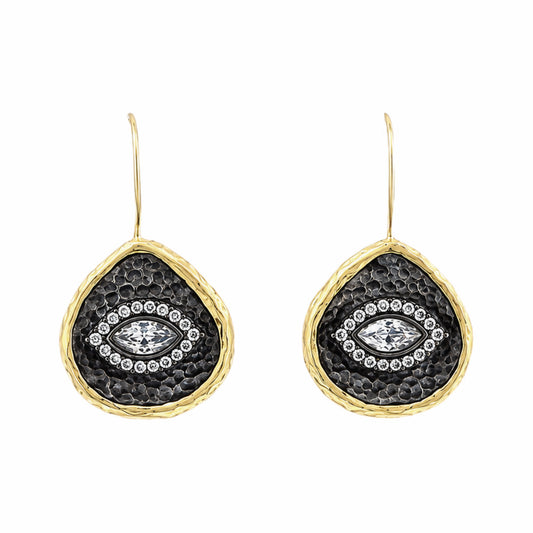 A pair of gold and dark silver teardrop-shaped drop earrings with a hammered gold finish, a textured center, and a central clear zircon evil  eye gemstone surrounded by small clear stones, on white background.