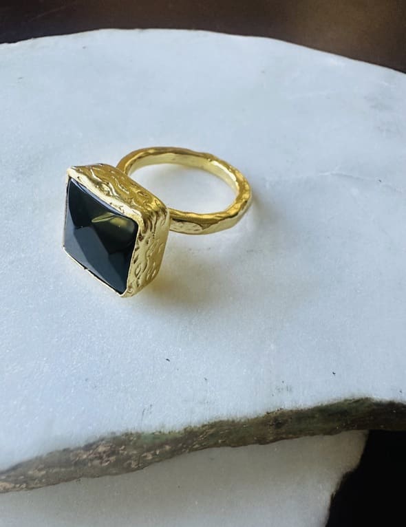 Handmade sustainable gold-plated onyx ring facing left on a white marble surface 