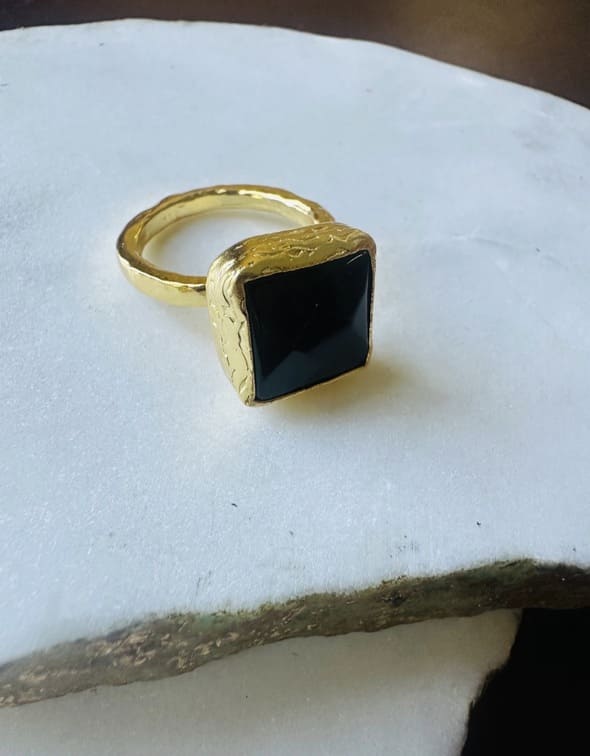Handmade eco-friendly gold-plated square onyx ring facing right on white marble surface 
