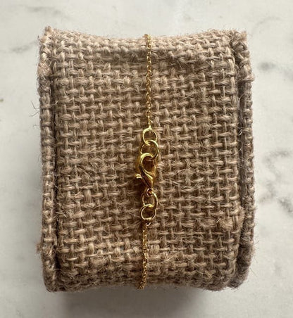 Gold bracelet back on a textured beige fabric with a marble background