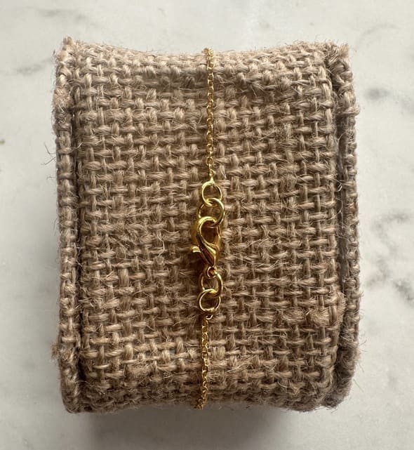 Back of Gold minimal bracelet on a textured beige fabric with a marble background