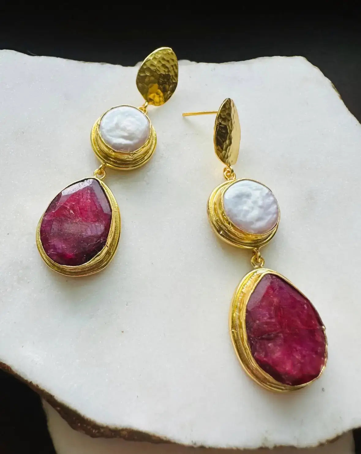 Elegant handmade gold-plated ruby and flat pearl dangle earrings arranged on white surface 