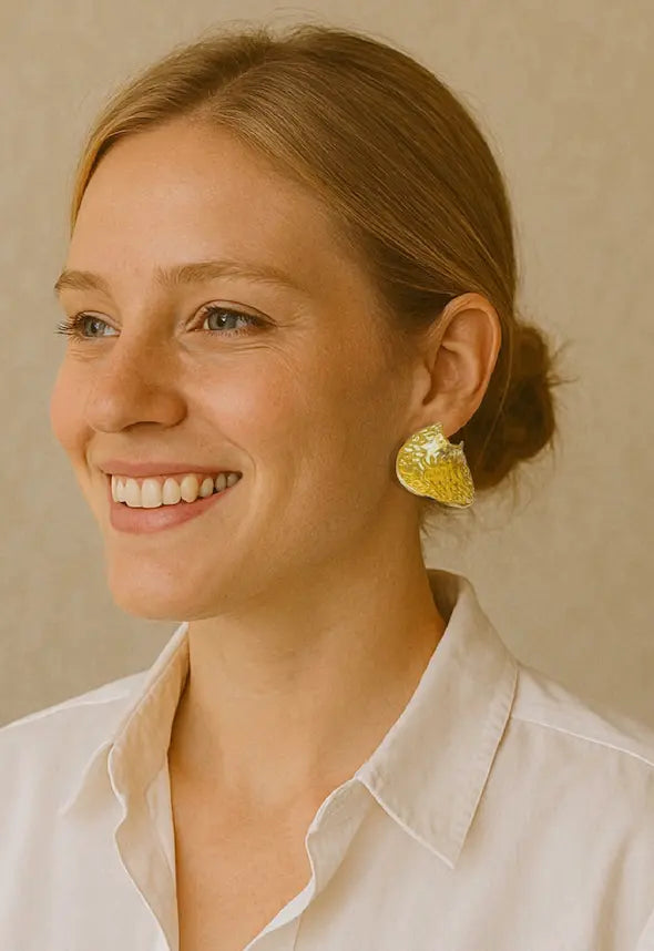 Woman wearing white dress shirt and handmade gold-plated contemporary statement  earrings against a beige background