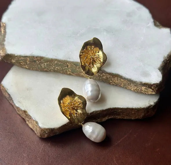 Handmade sustainable gold-plated flower and baroque pearl earrings on a white marble