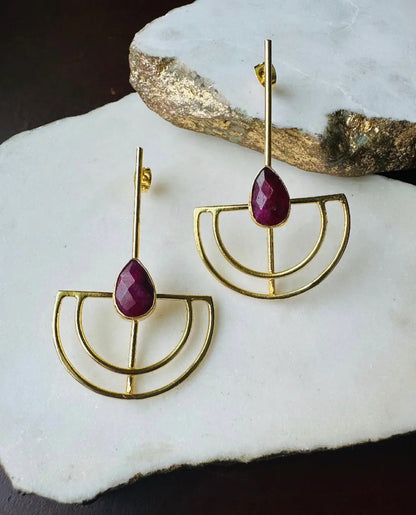 Contemporary Gold-plated earrings with ruby gemstones on a white stone surface