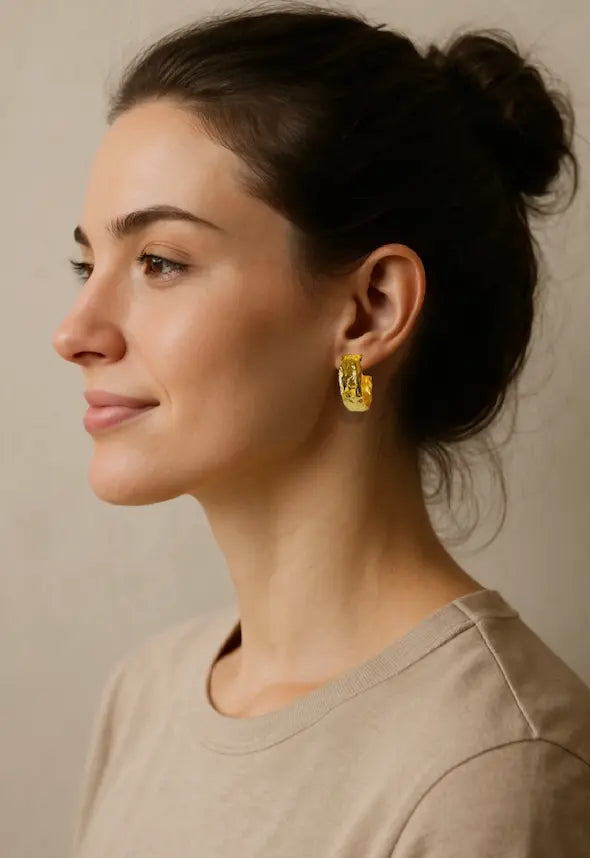 Woman wearing gold-plated artisanal textured hoop earrings with a neutral background